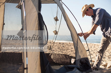Man setting up tent on beach, Malibu, California, USA