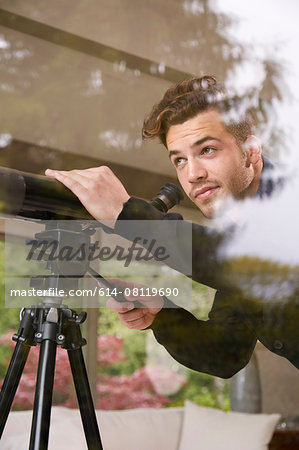 Portrait of man using telescope looking out of window