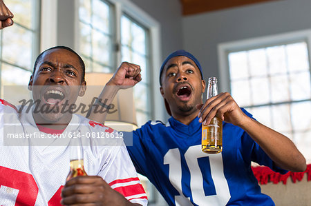 Two male friends celebrating whilst watching TV from sofa