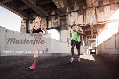 Female and male runners running under city bridge Female and male runners running under city bridge