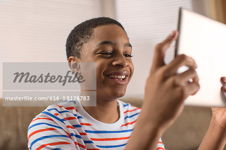 Teenage boy posing for digital tablet selfie on sofa