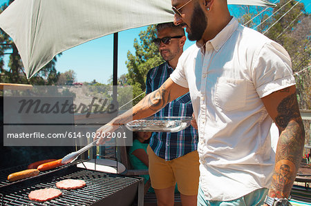 Two mid adult brothers barbecuing in garden