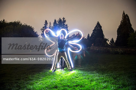 Two men standing together in field at dusk, creating star shape with bodies, friend tracing body shape with light trail