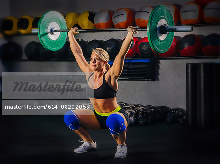 Young woman squatting with barbell raised in gym