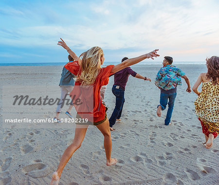 Group of friends walking along beach, young woman with arms in air, rear view