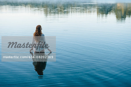 Rear view of young woman in lake rippling surface with her fingers