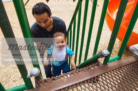 Young man guiding toddler brother up playground slide steps