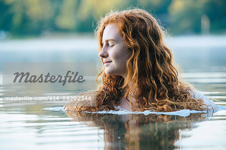 Head and shoulders of beautiful young woman with eyes closed in lake