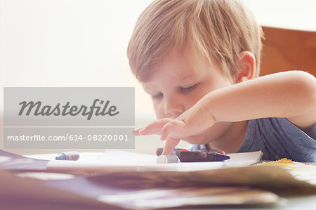 Boy sitting at table rolling crayons with finger, looking down