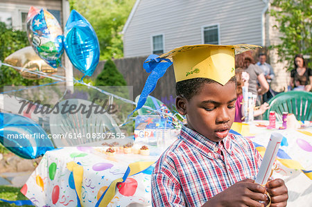 Young boy at kindergarten graduation, wearing paper mortar board, holding certificate