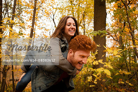 Young man giving girlfriend a piggy back through autumn forest