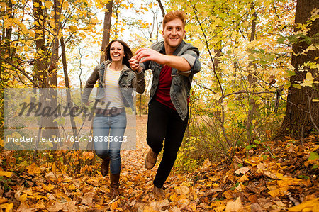 Romantic young couple running through autumn forest