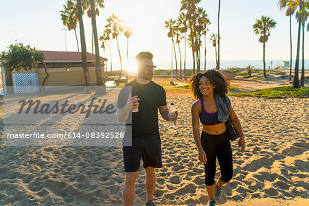 Couple wearing sports clothing, walking along beach, talking