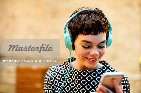 Mid adult woman, wearing headphones, looking at smartphone, smiling
