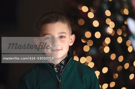 Portrait of boy in front of christmas tree looking at camera smiling