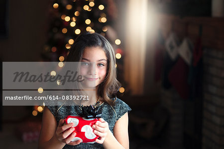 Portrait of girl in front of christmas tree holding gift looking at camera smiling