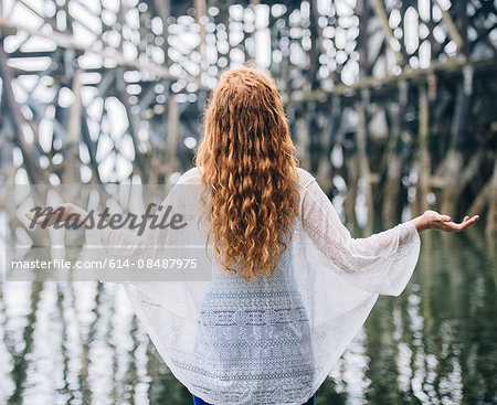 Rear view of woman with long red hair meditating in front of wood river pier