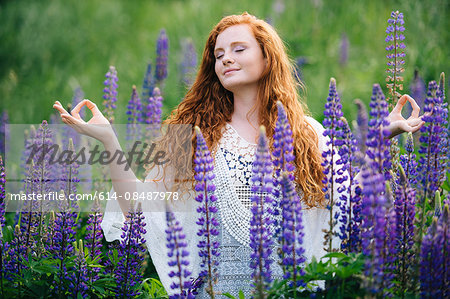 Serene young woman meditating amongst purple wildflowers