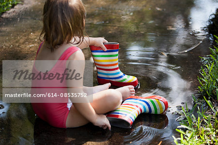 Child in wellies sitting in puddle of water