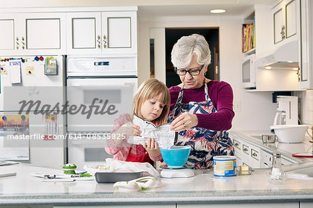 Girl and grandmother pouring cake mix at kitchen counter