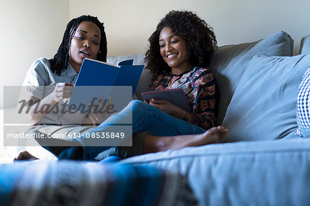 Lesbian couple relaxing sofa, reading book and using digital tablet