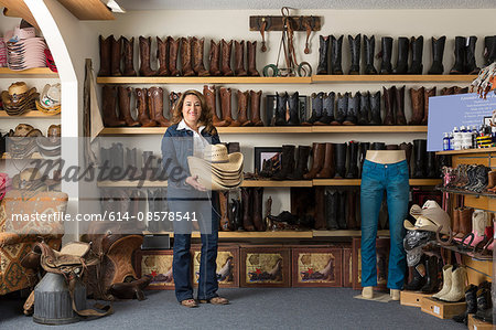 Shop assistant carrying stetsons in front of shelves of boots