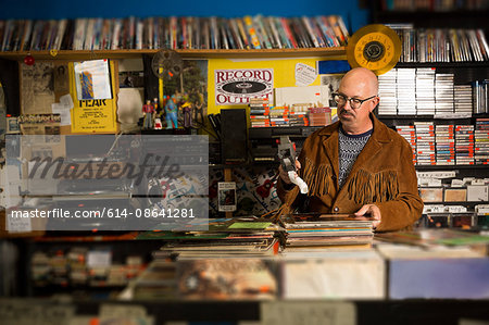Mature man in record shop, pricing up records using price gun