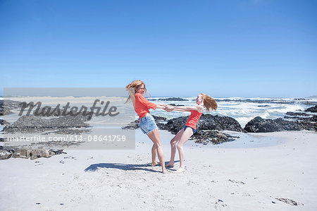 Girl and young woman holding hands and spinning each other around on beach, Cape Town, South Africa