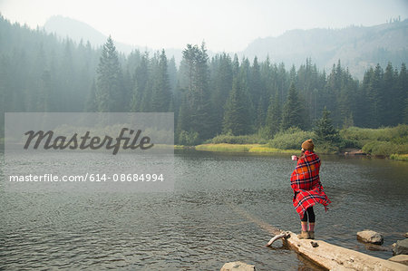 Woman wrapped in tartan blanket drinking coffee by misty lake, Mount Hood National Forest, Oregon, USA