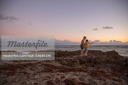 Girl and brother stepping over beach rocks at sunrise, Blowing Rocks Preserve, Jupiter Island, Florida, USA
