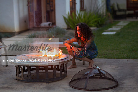 Mature woman crouching in front of patio fire at dusk