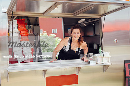 Portrait of woman leaning forward at hatch of food stall trailer