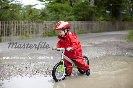 Smiling boy riding bicycle in puddles