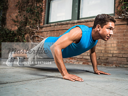 Young man doing push-up on city street