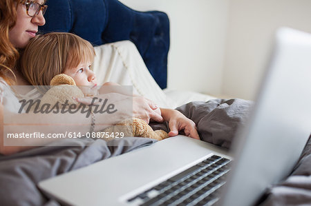 Mother and daughter lying in bed with laptop computer