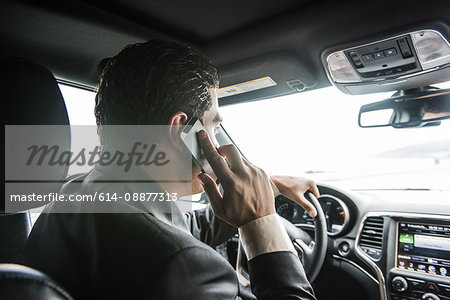 Over the shoulder view of young businessman driving whilst talking on smartphone