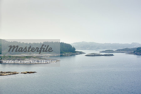 View across water of islands with fir trees and mountain range, Haugesund, Rogaland County, Norway