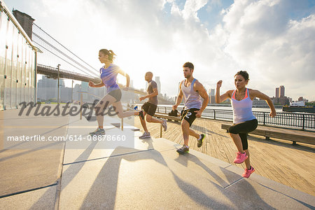 Four young adult running friends running up riverside stairs, New York, USA