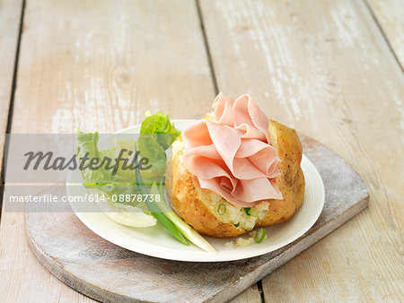 Wafer thin ham in baked potato with salad leaves and spring onions on white plate and whitewashed cutting board