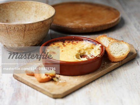 Bowl of welsh rarebit bake with toasted bread on wooden chopping board