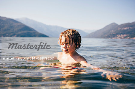 Mountain range and head and shoulders of boy in water arms open looking away, Luino, Lombardy, Italy
