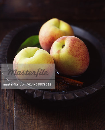 Peaches and leaves with cinnamon stick and star anise in vintage wooden bowl of water