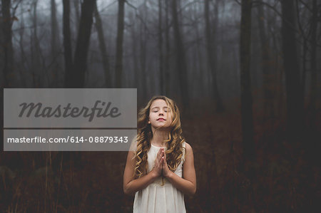 Portrait of long blond haired girl with eyes closed and hands together in misty forest
