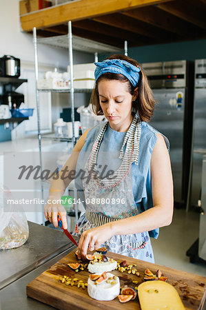 Woman preparing variety cheese plate with figs, nuts, pistachios, basil on wooden chopping board