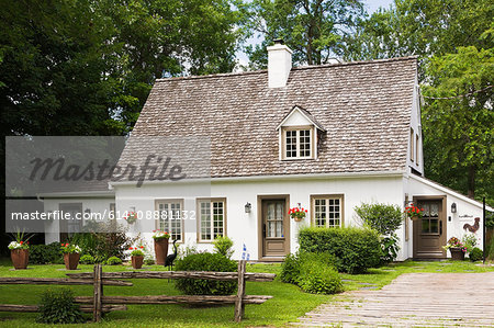 Old (circa 1886) white with beige and brown trim Canadiana cottage style home facade in summer, Quebec, Canada