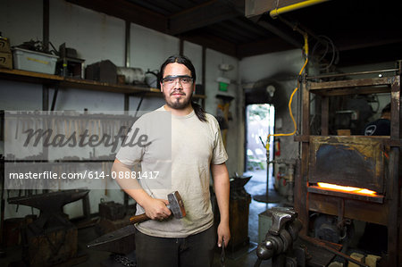 Portrait of male metalsmith by metal workshop furnace