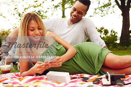 Male and female adult friends looking at smartphone at park picnic