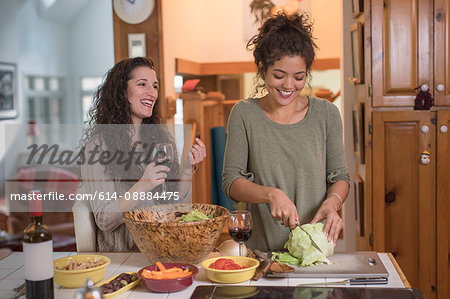 Two female friends preparing salad at kitchen counter