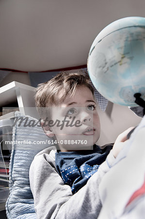 Boy lying in bed gazing at globe