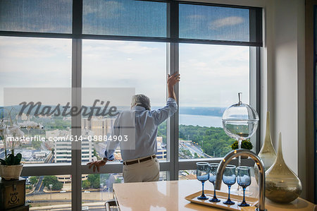 Senior man looking out of window of tall building, rear view